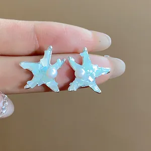 Macro view of starfish-shaped earrings with a central pearl and opalescent blue inlay