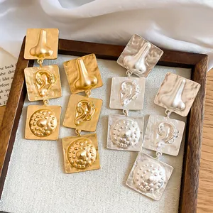 Detail of unique vintage earrings with sculpted nose and ear motifs in gold and silver.