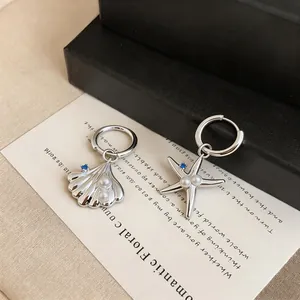 Detail view of asymmetric shell and starfish hoop earrings with pearls and blue zircon.