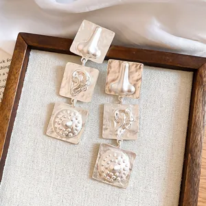 Detailed view of silver textured earrings featuring unique 3D facial feature embossments.