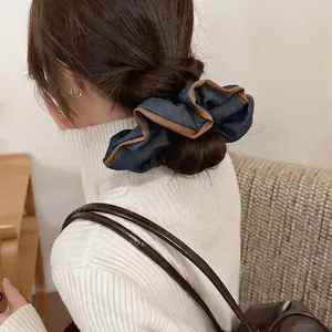 Close-up of a large denim fabric scrunchie with brown piping details on a model's hair