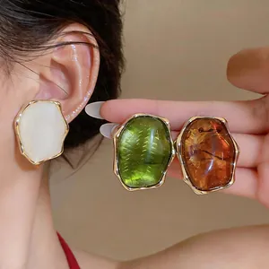 Close-up of irregular resin stud earrings in white, green, and amber Maillard colors
