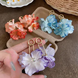 Hand showing colorful fabric flower drop earrings in orange, blue, and purple.