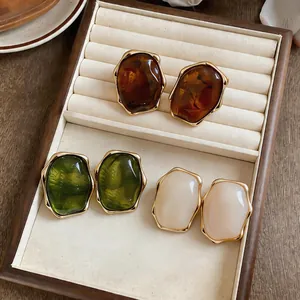 Detail view of stylish resin oval stud earrings in amber, green, and cream with gold borders