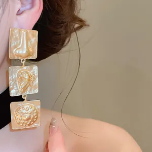 Detail view of unique matte gold earrings with nose and ear facial feature motifs
