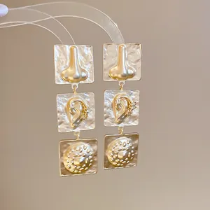 Detailed view of gold geometric earrings featuring unique 3D nose and ear designs on textured panels