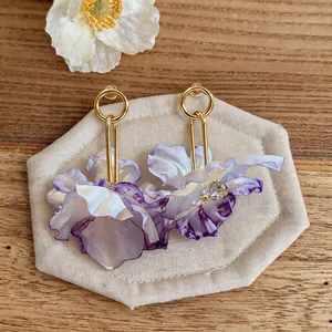 Detail view of purple fabric flower earrings with gold hooks on a neutral background