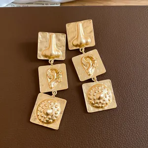 Macro detail view of vintage gold earrings with unique nose and ear relief designs