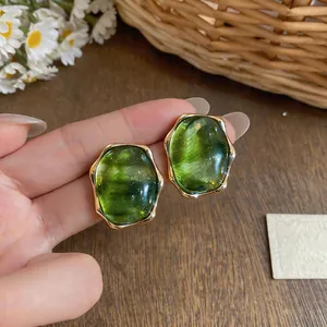Close-up shot of green resin oval stud earrings featuring elegant gold-tone metal frames