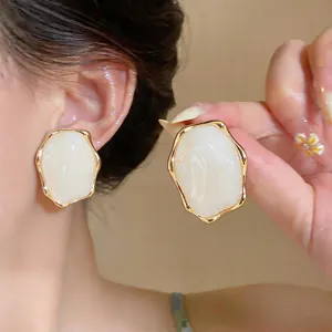 Detail view of irregular oval resin stud earrings with gold pleated edges on model.