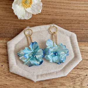 Close-up of blue fabric flower earrings with gold finish on a rustic wooden background.