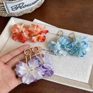 Macro view of oversized fabric flower earrings in purple, blue, and orange colors.