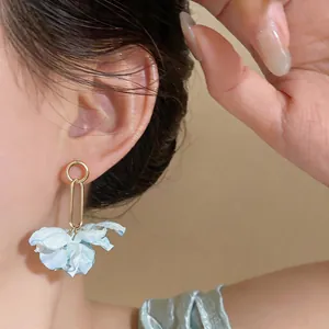 Detail of a light blue fabric flower drop earring worn by a model for a beach vacation look.