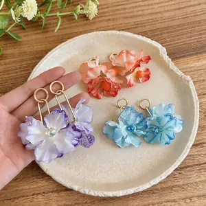Hand-held view of three pairs of oversized fabric flower earrings in purple, blue, and orange