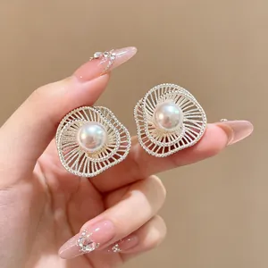 Detailaufnahme von eleganten, hohlen Blumenohrringen mit Perlen, die in der Hand liegen