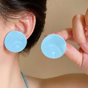 Detailed macro view of light blue wrinkled round stud earrings worn on a model's ear