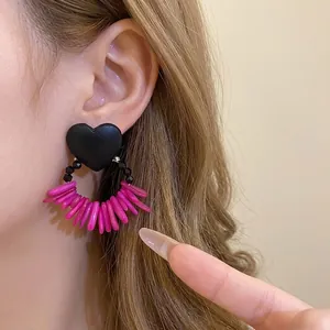Retro black heart stud earrings with pink shell tassels shown on a model's ear.