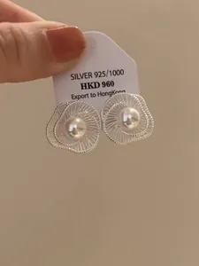 Detailansicht von hohlen Blumenohrsteckern mit Perle auf einem silbernen Etikett