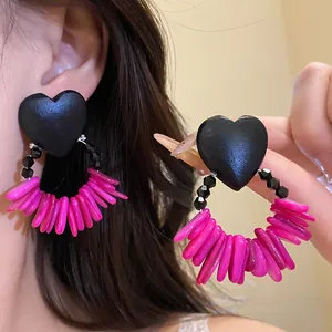 Close-up view of vintage heart-shaped wooden earrings with fuchsia pink shell tassels