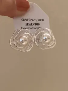 Makro-Detailansicht eleganter silberner Blumenohrringe mit Perle auf einem Display-Etikett