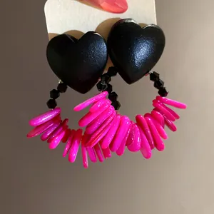 Close-up of retro heart earrings with wood texture and hot pink shell tassels.