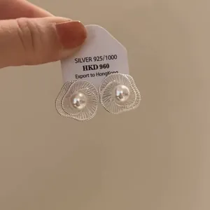 Detailansicht von silbernen hohlförmigen Blumenohrringen mit Perle auf einem Etikett