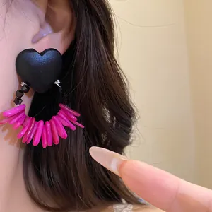 Detail view of retro black heart stud earrings with vibrant magenta shell tassels.