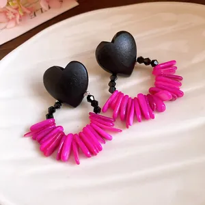 Close-up of retro heart wood earrings with pink shell fringe on a white textured plate.