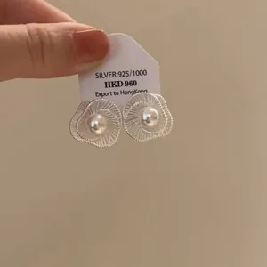 Detailansicht von hohlen silbernen Blumenohrsteckern mit einer zentralen Perle auf einem Etikett.
