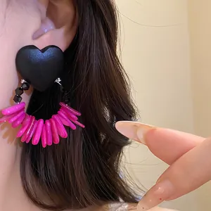 Detailed view of retro black heart wood earrings with pink shell tassels worn on ear