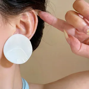 Close-up view of a large white irregular round stud earring worn on a model's ear