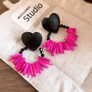 Macro view of retro heart wood and vibrant pink shell tassel earrings on canvas bag