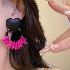 Detailed macro view of retro black heart earrings with vibrant pink wooden shell tassels