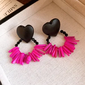 Detailed view of vintage heart wood earrings featuring vibrant magenta shell tassels