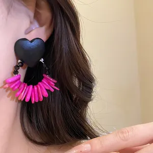 Detailed close-up of retro wooden heart earrings featuring vibrant pink shell fringe tassels.