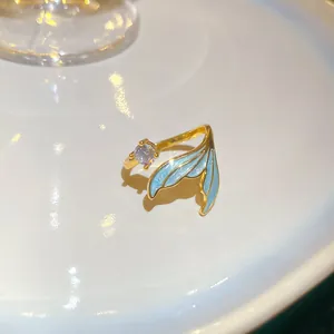Close-up of a gold mermaid tail ring with blue enamel and sparkling zircon