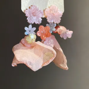 Vista ravvicinata dei fiori in resina rosa e petali di chiffon su dolci orecchini pendenti.
