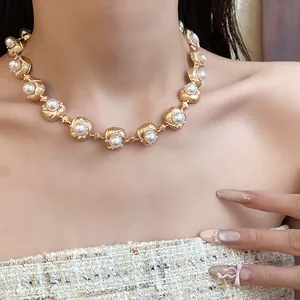 Close-up detail of a vintage court style gold necklace with pearls on a model wearing tweed