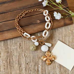 Close-up of retro gold-toned flower pendant and chunky white chain necklace