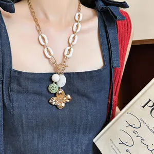 Detail view of retro gold flower pendant necklace with white chain links on model