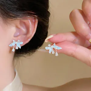 Detalle de pendientes de flor en esmalte azul con perlas y circonitas en una modelo