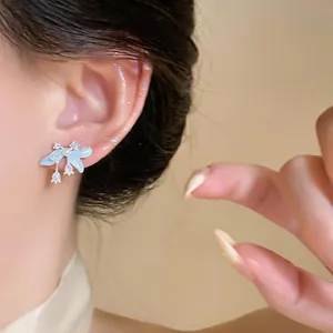 Primer plano de pendientes flor esmalte azul claro con circonitas y detalles de perlas.