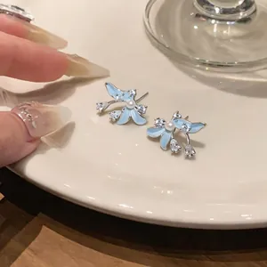 Pendientes de flores azules con perla y circón sobre un plato blanco