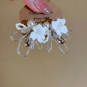 Detailed view of French style white floral stud earrings with pearls and beads