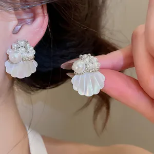Close-up detail of elegant white pearl and shell flower stud earrings worn on the ear