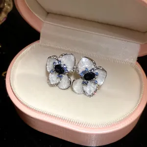 Primo piano di orecchini a fiore in smalto bianco con gemme blu in scatola rosa