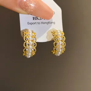 Vista detallada de pendientes dorados en forma de C con perlas y diseño de encaje filigrana