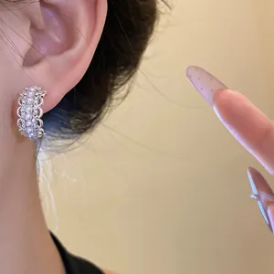 Primer plano de elegantes pendientes plateados en forma de C con perlas y strass en la oreja