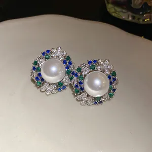 Detailed view of vintage-style pearl stud earrings with green and blue zircons