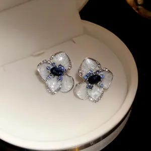 Dettaglio di eleganti orecchini a lobo a fiore con smalto bianco e cristallo blu
